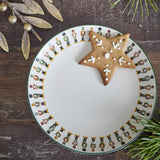 Jolly Stoneware Christmas Side Plate in cream with a ring of nutcracker soldiers around the rim, shown with a star-shaped cookie, styled on wood with gold foliage.