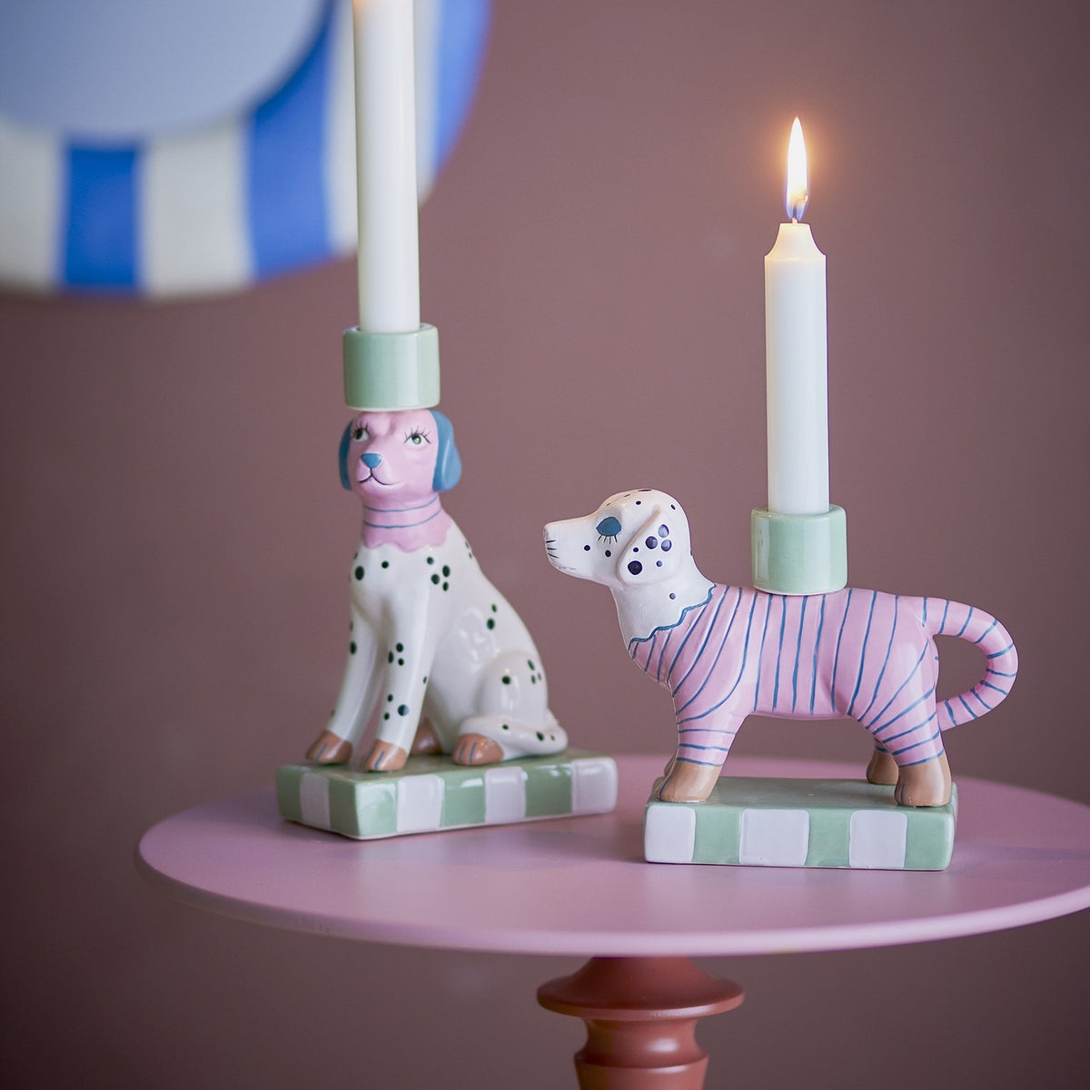 Doglie Striped Stoneware Candle Holders Set of 2 in pink, dog-shaped ceramic candle holders on checkered bases, shown with white candles on a pink side table.
