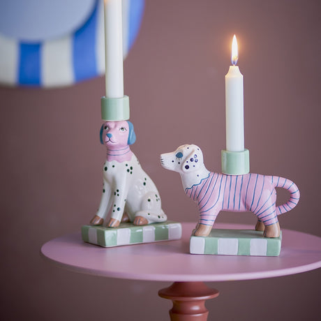 Doglie Striped Stoneware Candle Holders Set of 2 in pink, dog-shaped ceramic candle holders on checkered bases, shown with white candles on a pink side table.