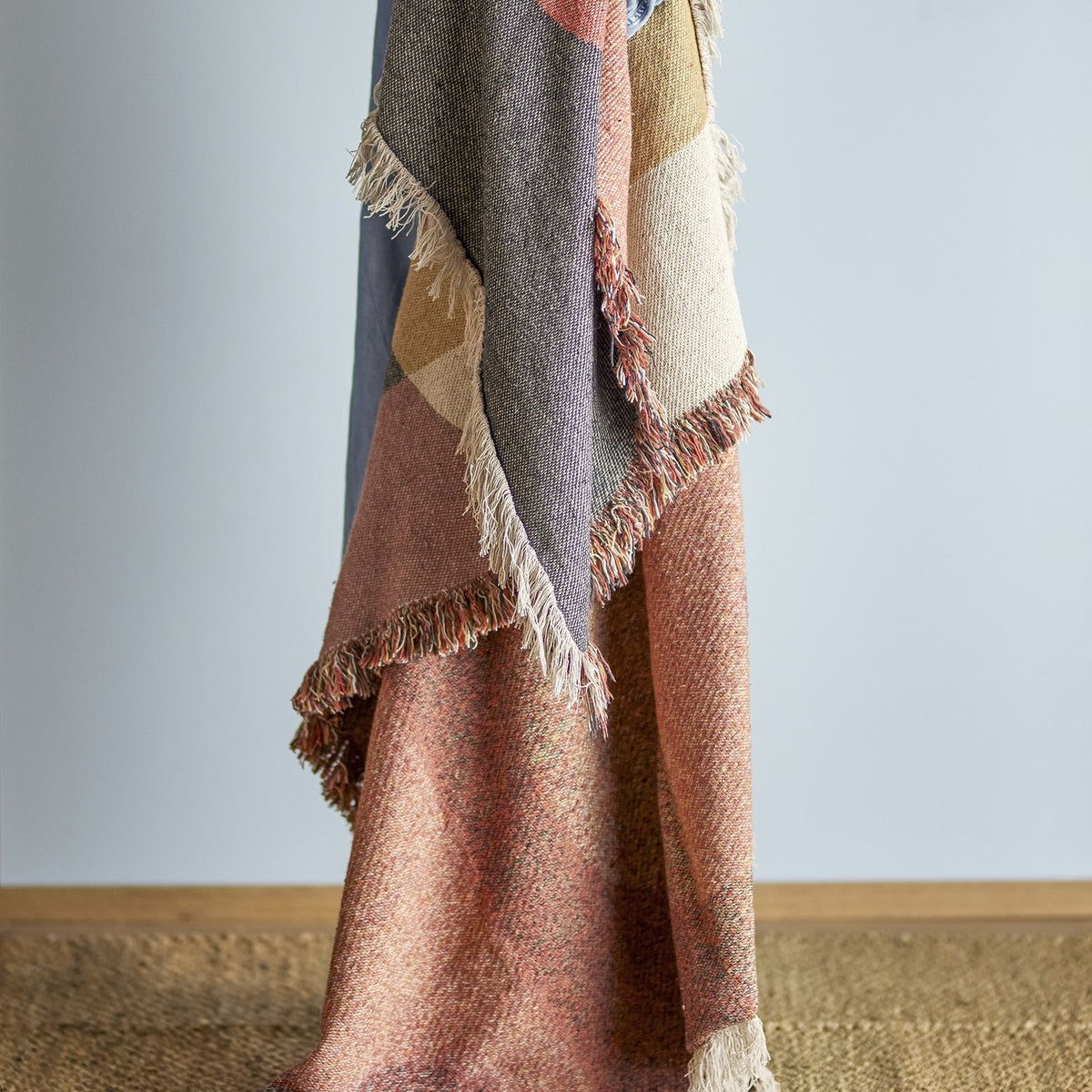 Arni Throw in Multi draped vertically, showing a woven curved colour-block design in grey, pink, tan and cream with a thick mixed-yarn fringe, against a plain light background.