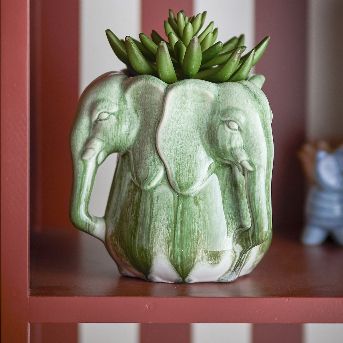 Pontus Stoneware Vase 15.5cm in green, shaped as a ring of elephant heads with trunk handles, holding a succulent on a red and white striped shelf.