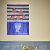 Florinda Striped Wooden Framed Print in Multi, showing a painterly bouquet of peach flowers in a striped vase against green and white stripes with a blue tabletop band.