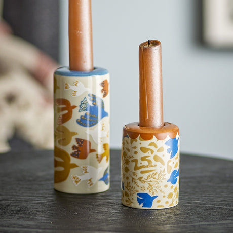Anniversary Floral Stoneware Candle Holders, set of 2, slim cylindrical ceramic in multicoloured bird and floral pattern, holding taper candles on a dark surface.