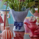 Belivia Bouquet Stoneware Vase 28.5cm in blue, with wavy petal-like rim and a navy polka-dot bow at the base, shown with flowers alongside other decorative vases.
