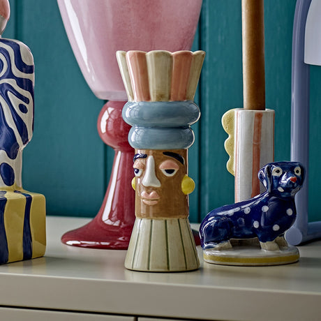 Minio Ceramic Vase 17cm in multicoloured stripes, featuring a sculpted face with earrings beneath a scalloped petal rim, displayed among other decorative vases.