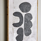 Comma Wooden Framed Print in Black, featuring four textured black forms—a round pebble, a bracket curve, and two stacked lobes—on a brushed white canvas with a slim firwood frame.