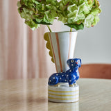 Multicoloured striped stoneware vase, 21.5cm, with scalloped fin design beside a polka-dot dachshund figure on a striped base, styled with green hydrangeas on a wooden table.