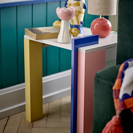 Banjo Side Table in Multi, a square MDF side table with a white top on mismatched legs including a yellow post, pink panel and tall blue board, styled with decor in a living room.