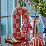 Mae Ceramic Vase 32cm in Orange, a tall ceramic loop vase with handpainted orange and white check pattern, styled on a table with a pink glass lamp and small striped vase.