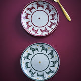 Siffer stoneware Christmas plates, set of 2, scalloped rims, red plate with horses and hearts, green plate with horses and stars, shown with a gold spoon.