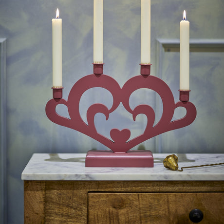 Salia Heart Advent Candle Holder in red MDF, a heart-shaped cut-out design with scrolls and four lit candles, displayed on a marble-top wooden cabinet.