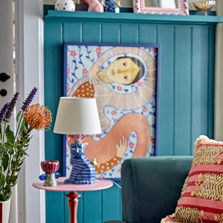 Floriesta Floral Wooden Framed Print in multi tones, shown mounted on a teal panelled wall above a side table with lamp in a living room setting.