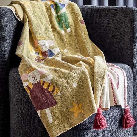 Peo Striped Christmas Throw in green, draped over a grey armchair, showing mice-in-angel-costume motifs with stars on one side and a red-striped reverse with tasselled corners.