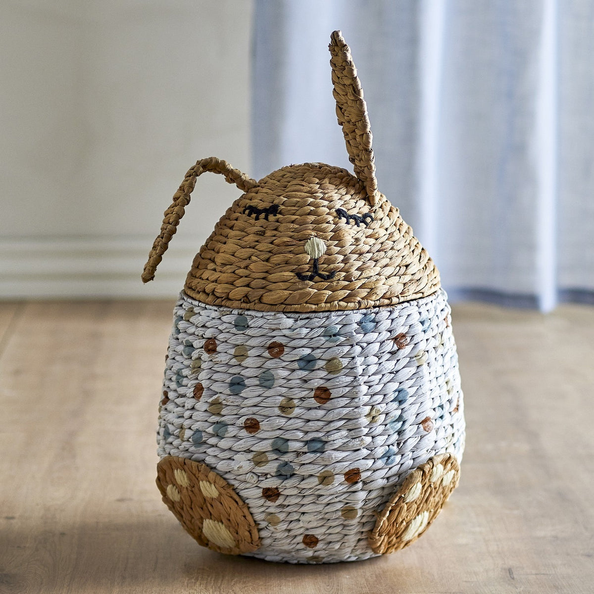 Villja rabbit-shaped kids storage basket in water hyacinth, with a sleeping-face lid, two braided ears, and a dotted multicoloured egg-shaped body with paw feet.