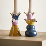Swift Bird Stoneware Candle Holders, set of two ceramic pieces with dotted birds beneath leaf-patterned flower cups, one on a mustard cone base, the other on a blue tiered base, holding taper candles.