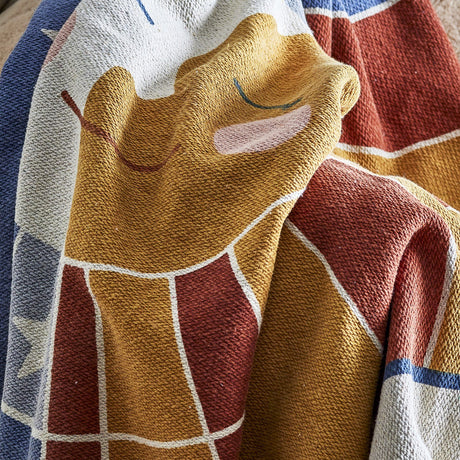 Sun Cotton Throw in multicoloured woven cotton blend, close-up of a smiling sun face with closed eyes and rounded cheeks, draped in folds with star and grid patterns visible.