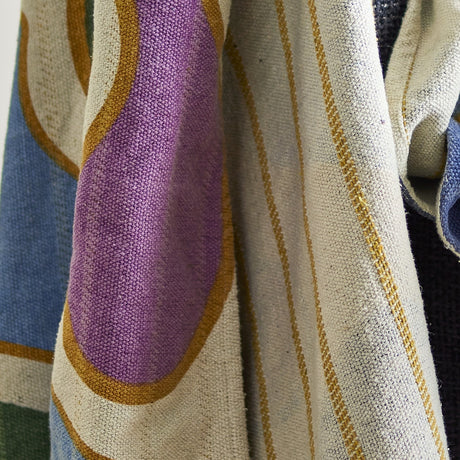 Salacia Throw in multicoloured woven fabric, draped to show a curved purple band with mustard outline alongside cream ground and fine striped detailing.