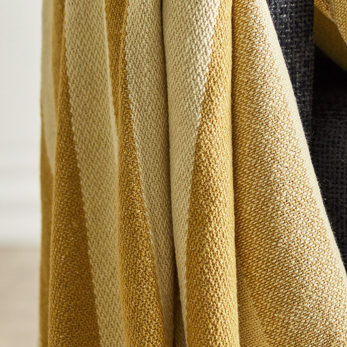 Frello Striped Cotton Throw in yellow, draped in folds showing alternating deep and pale yellow woven stripes with a textured cotton blend finish.