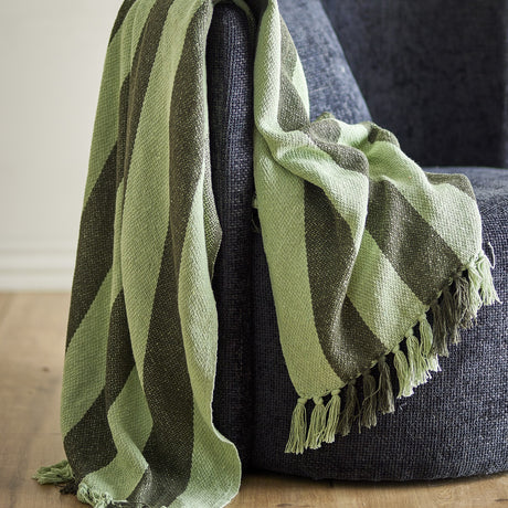 Frello Striped Cotton Throw in green, a broad-stripe woven blanket with knotted tassels, draped over a dark grey armchair.