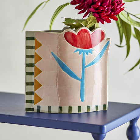 Vinia Floral Stoneware Vase 23cm in multi, hand-painted with a red flower on blue stem and leaves, striped and triangle borders, shown on a blue table with a flower display.
