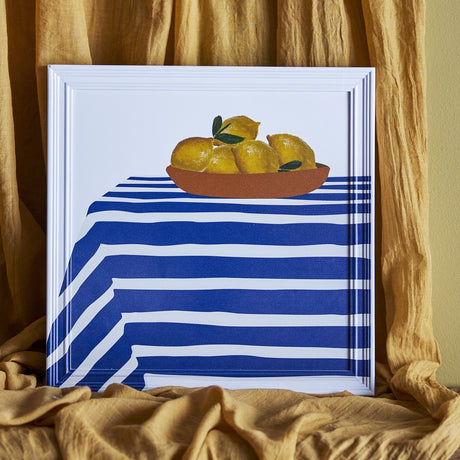 Limone Striped Wooden Framed Print 40x40cm, square wall art showing a bowl of lemons on a blue and white striped cloth, white wood frame, shown against draped gold fabric.