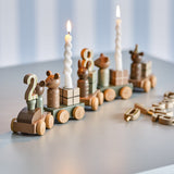 Junaid Dark Brown Birthday Decoration wooden train with number pegs, animal figures, gift block carriages and candle holders with lit spiral candles, on a light grey surface.