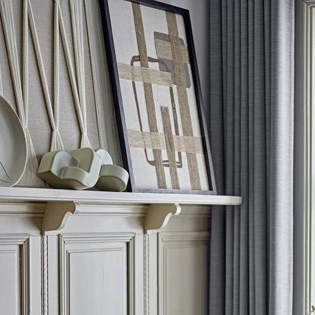 Bie Geometric Cotton Wall Decor in beige, framed textile art with woven jute bands forming a grid over rounded and square outlines, shown on a mantel shelf.