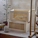 Piana Wooden Storage Boxes Set of 2 in natural pine with woven rattan side panels, stacked on a wooden table beside a plant and clothing rack.