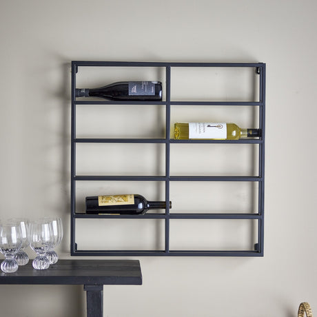 Magne Iron Wine Rack in black, a square wall-mounted grid frame with slim iron bars forming two columns of open shelves, holding three wine bottles above a dark console table.