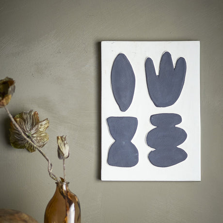 Lutton Stoneware Wall Decor in white, a rectangular panel with four raised organic shapes in grey, shown mounted on a sage green wall beside a dried floral arrangement.