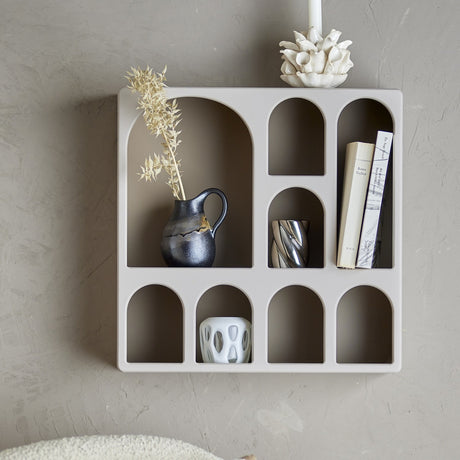 Graphia Bookcase in grey, a wall-mounted MDF shelving unit with arched compartments, shown holding books, a jug vase, and small decor pieces against a plain wall.