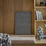 Rivalta Pin Board in black with a woven diamond pattern, leaning against a wood-panelled wall near a bookshelf and upholstered bench.