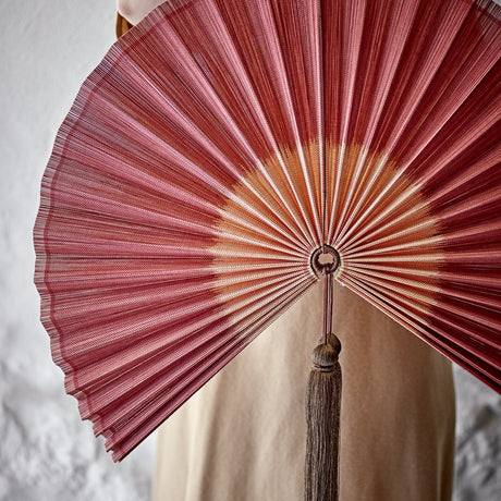 Jaime Bamboo Wall Decor in pink, a pleated fan-shaped wall art piece with ombre shading and a hanging tassel at the hub, shown against a light grey background.