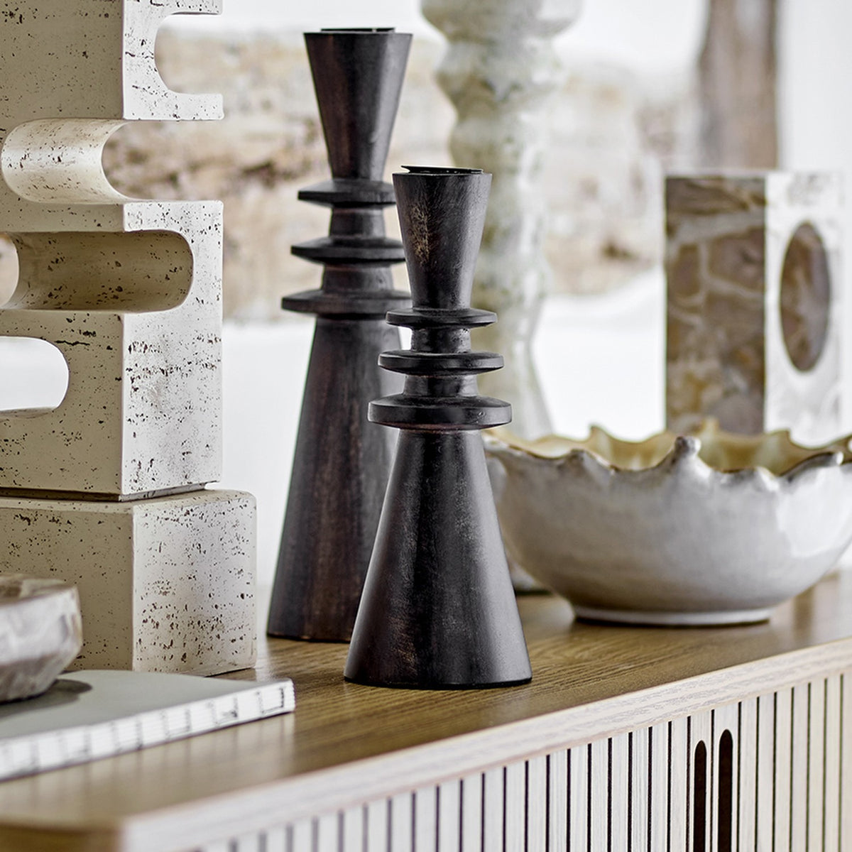 Armel Wooden Candle Holder in black mango wood, 20cm tapered cone design with stacked flat rings, shown on a sideboard beside a ceramic bowl and decorative objects.