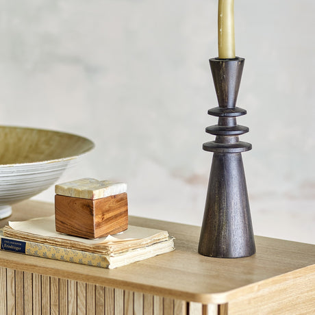 Armel Wooden Candle Holder in black, 26cm mango wood with stacked ring details, holding a taper candle on a wooden sideboard beside books and a bowl.