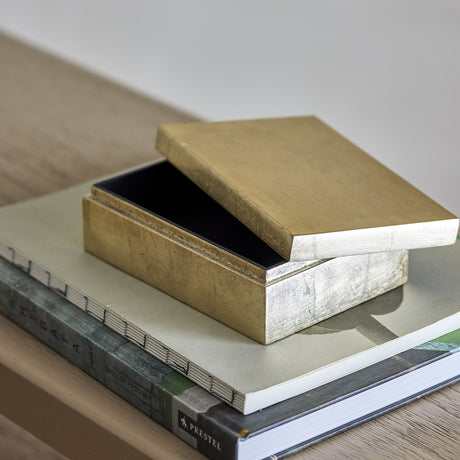 Nenon rectangular storage box with lid in gold MDF with a high-gloss finish, shown open with black interior, resting atop stacked books.