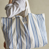 Trina Striped Cotton Shopping Bag in blue, carried over the shoulder, showing vertical stripes, long fabric handles and a fabric brand label on the front.