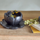 Reiko black marble flower tealight holder with petal-edged bowl on a matching flower-shaped tray, shown on a wooden surface with dried foliage.