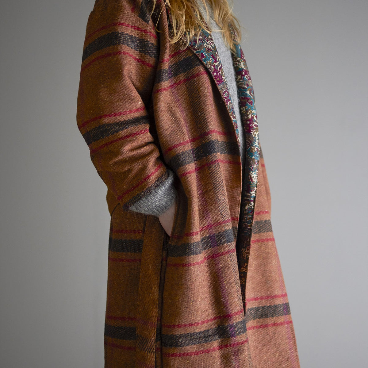 Rieti Kimono in brown, worn open over a grey top, showing woven striped fabric with a printed floral reverse visible at the lapel, against a plain grey background.