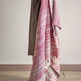 Oia Snowflake Cotton Christmas Throw in red, woven with striped and snowflake patterns and knotted tassel fringe, draped over a chair against a plain light background.