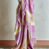 Isnel Striped Throw in pink and yellow woven stripes with knotted tassel fringe, draped over a chair against a plain light background.