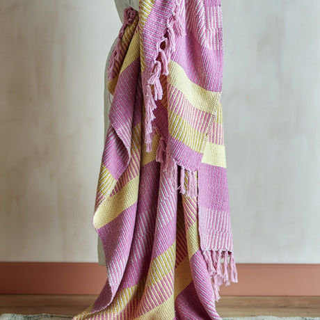 Isnel Striped Throw in pink and yellow woven stripes with knotted tassel fringe, draped over a chair against a plain light background.