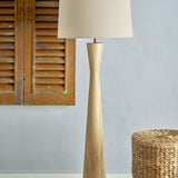 Leonor Wooden Floor Lamp with Linen Shade in Natural, featuring a tapered rubberwood column with a pinched waist and a tapered linen drum shade.