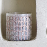 Esther Glass Tealight Holder in pink, a cylindrical holder with a frosted granular texture and raised chevron lattice pattern, displayed in a wall niche.