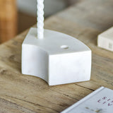 Florida Marble Candle Holder in white, a curved low block with twin candle holes, shown holding a twisted taper on a wooden table.