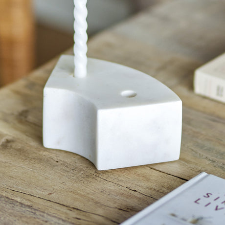 Florida Marble Candle Holder in white, a curved low block with twin candle holes, shown holding a twisted taper on a wooden table.