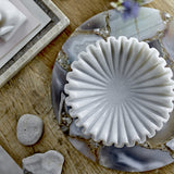 Harmonia Marble Bowl 17.5cm in white with ribbed, flower-like fluted edges, shown on an agate and wood table beside pebbles and stacked trays.