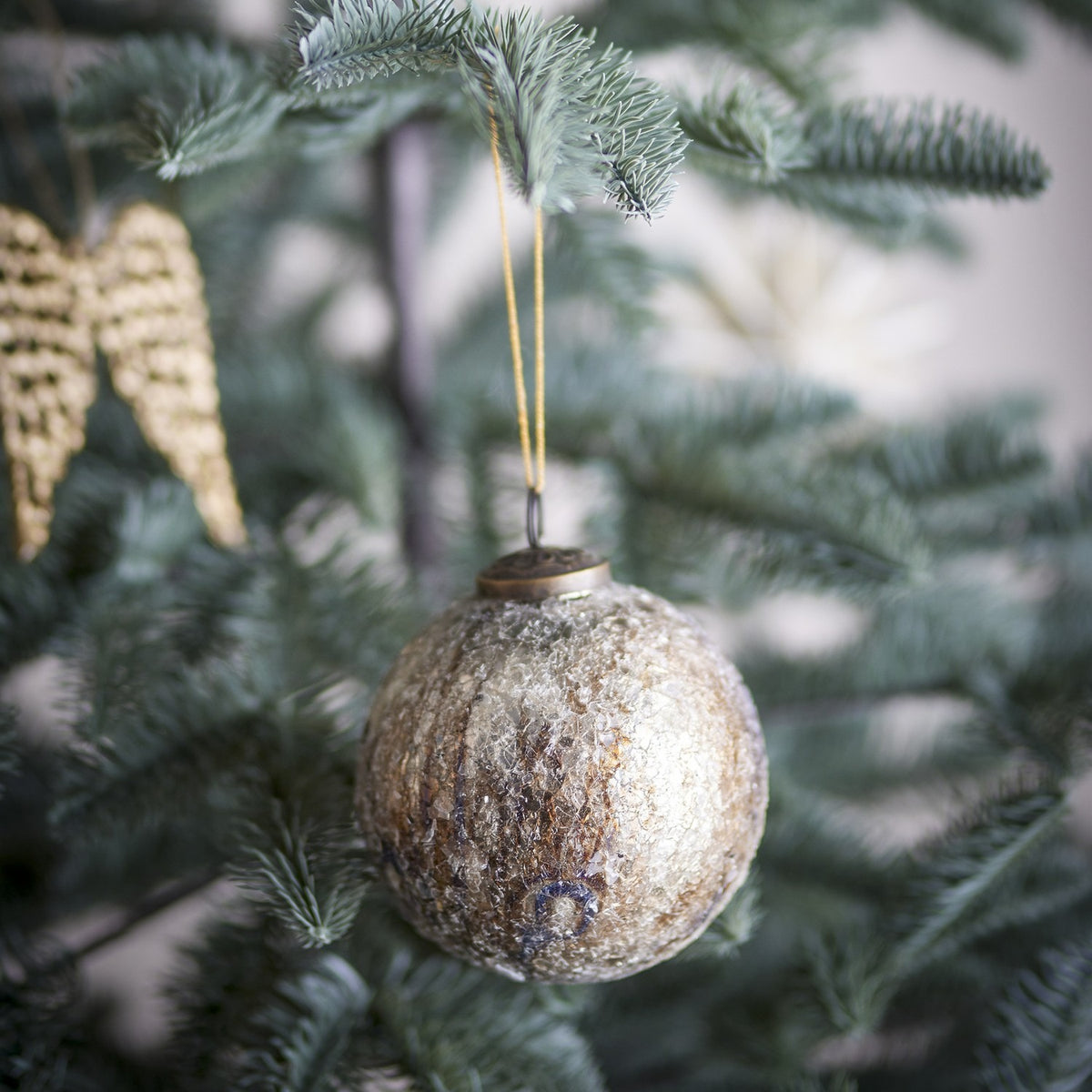 Nany Glass Christmas Bauble in bronze, a round 10cm ornament with crackled, crazed glass texture and a metal cap and loop, hanging from a Christmas tree branch.