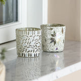Myr glass tealight holders, set of 2, white mosaic design with leaf pattern and star motif, shown on a marble surface by a window.