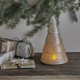 Emilius glass Christmas tree decoration in white, tiered fir shape with textured crackle finish, lit from within and displayed on a wooden surface with gifts and festive greenery.